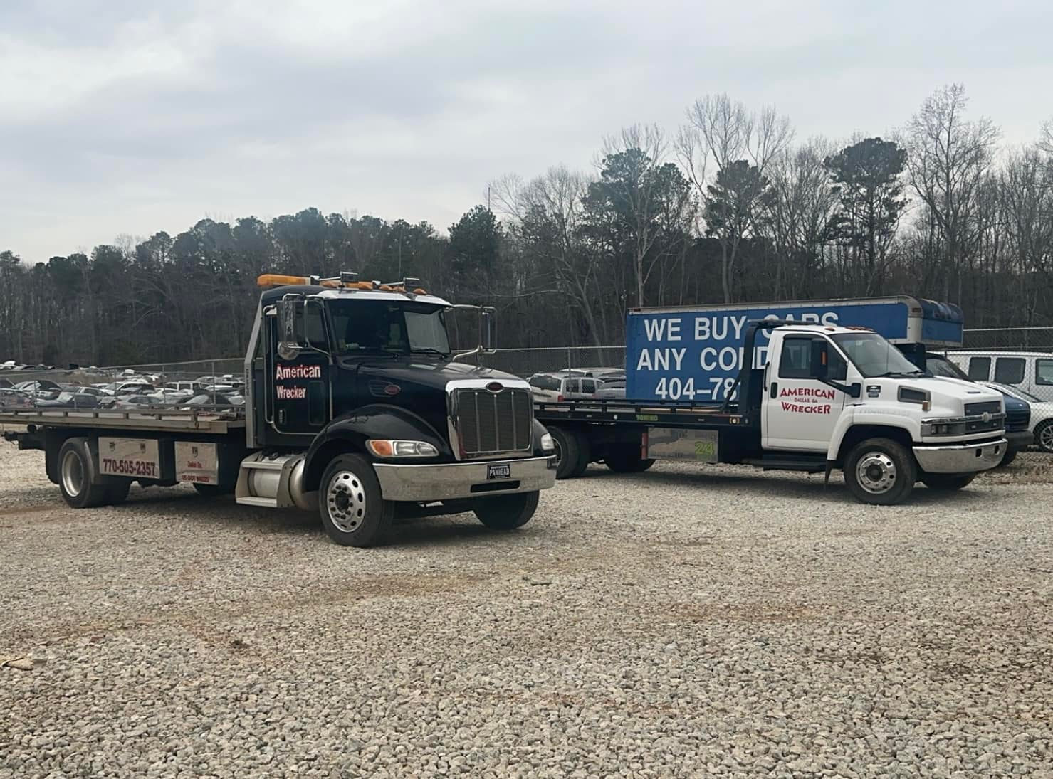 Two American Wrecker rollback tow trucks parked in the yard